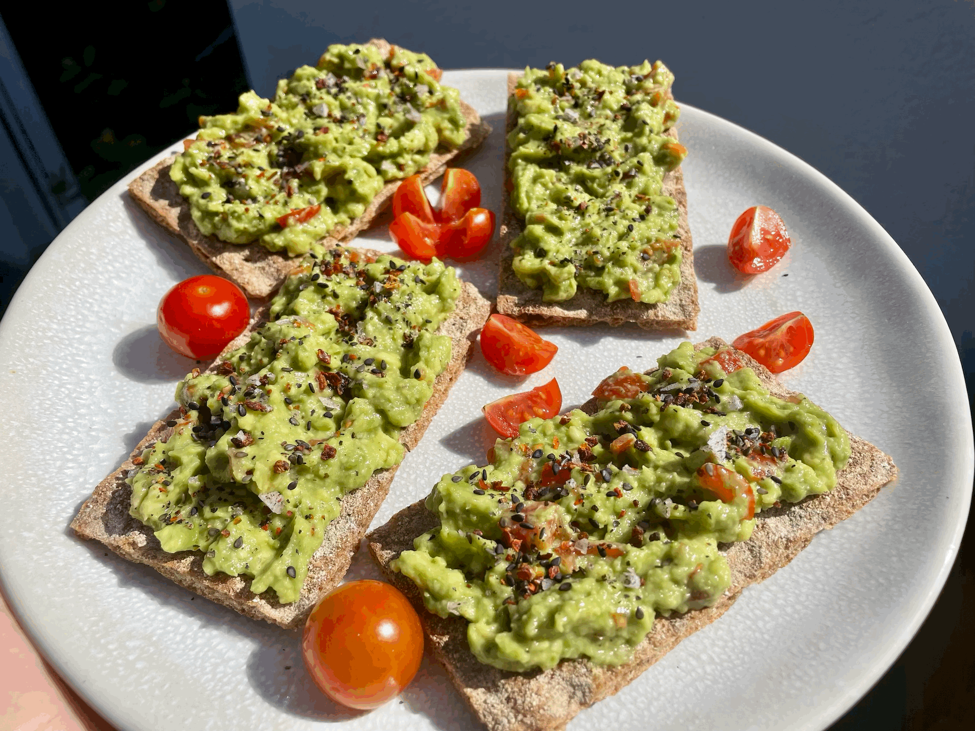 Vier Knäckebrote mit Guacamole belegt und Tomaten verziert.