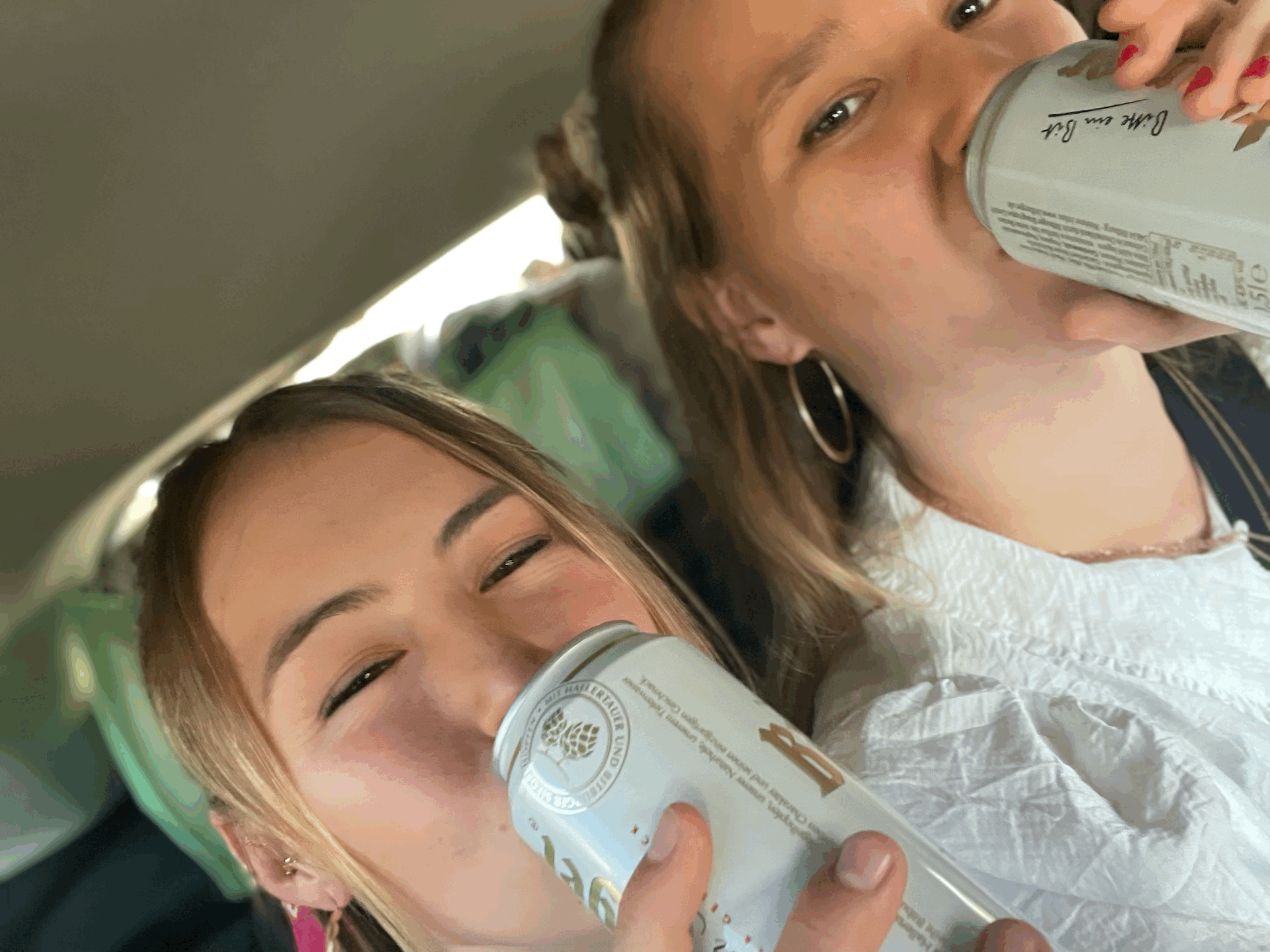 Das bild wurde in einem Auto geschossen. Zwei Frauen sitzen mit einem Dosenbier auf der Rückbank. Sie sind dezent geschmink und die Haare sind halb offen.