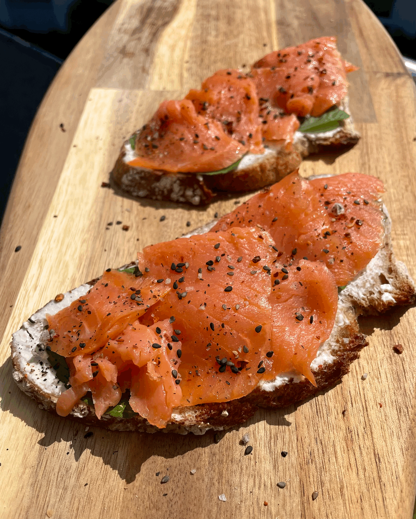 Belegtes Brot mit Merretich-Frischkäse, Minzblättern und Räucherlachs auf einem Brett. 