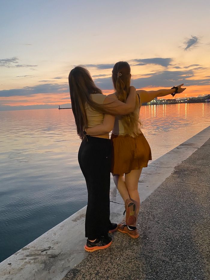 Zwei Frauen stehen bei Sonnenuntergang an der Hafenmauer mit Blick aufs Wasser.