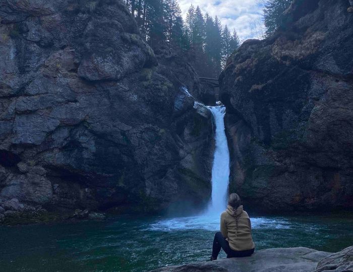 Eine junge Frau mit dem Rücken zum Betrachter blickt auf einen Wasserfall.