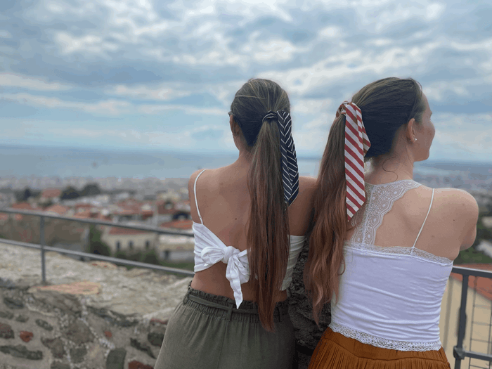 Zwei junge Frauen stehen mit dem Rücken zum Betrachter. Ihr Blick ist auf die Stadt Thessaloniki und das Meer gerichtet.