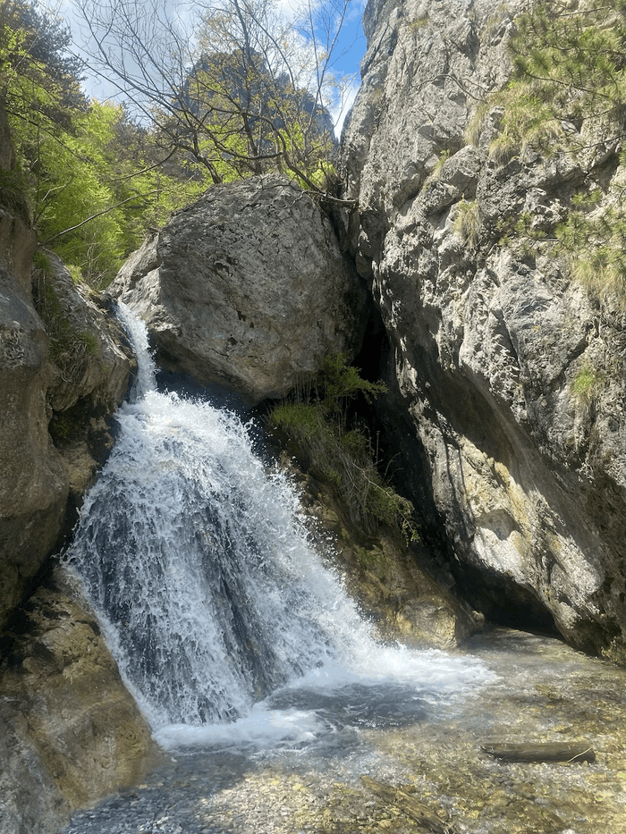 Ein Wasserfall ergießt sich in ein Felsbecken. Die Sonne scheint.