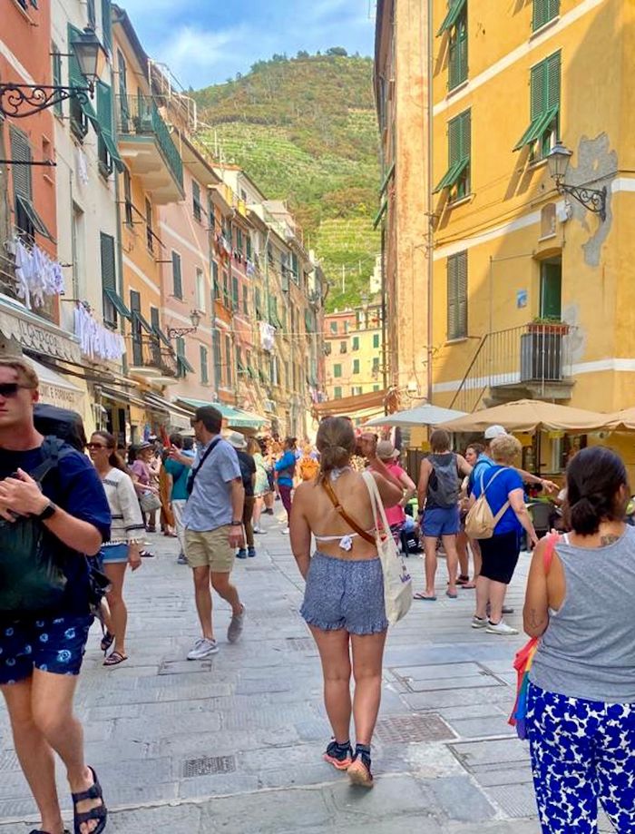 Eine junge Frau in kurzer Hose und Bikini-Oberteil läuft durch die bunte, belebte Innenstadt von Vernazza.