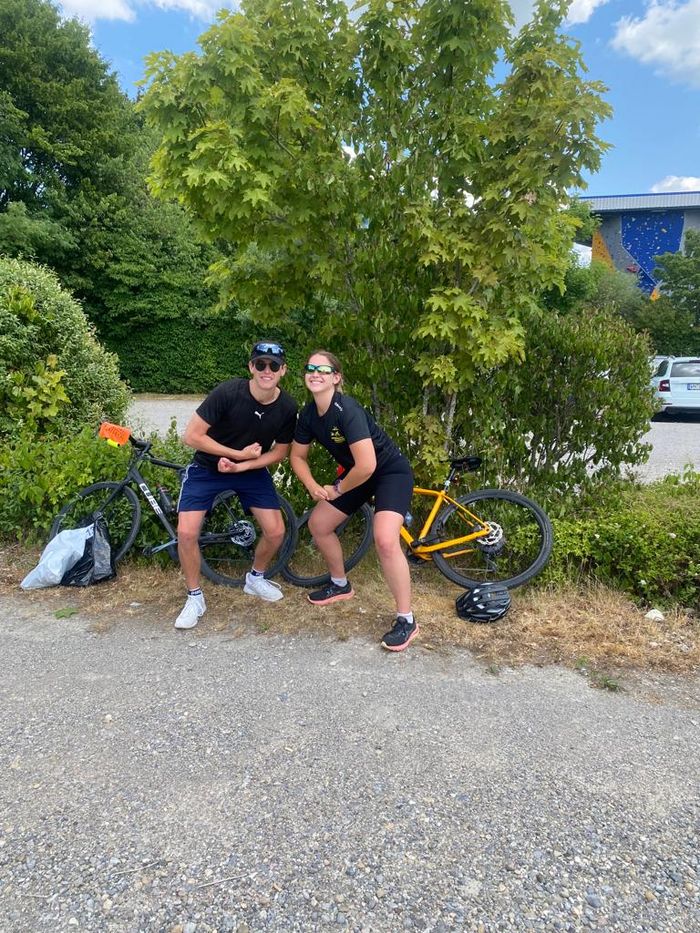 Mann und Frau posieren stolz vor ihren Rennrädern. Beide Tragen Sportkleidung und -sonnenbrillen.