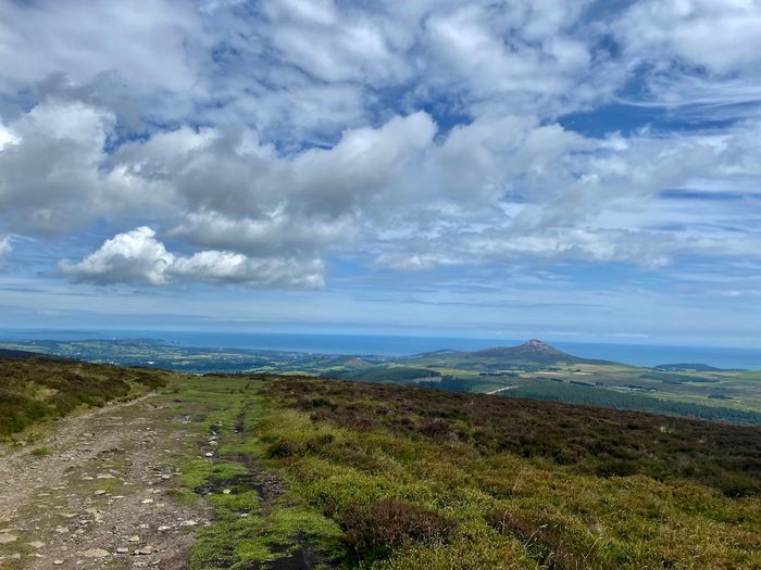 Aussicht von einem Gipfel entlang des Wicklow Ways auf die umliegenden Weideländer, Berge und das irische Meer.